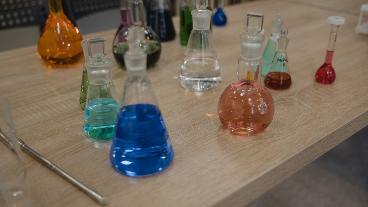 Colorful laboratory flasks with various liquids on a wooden desk for science experiments.